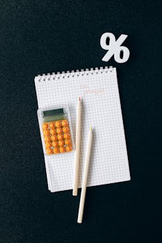 Flat lay of a colorful calculator, notebook, and pencils on a black background with a percent sign.